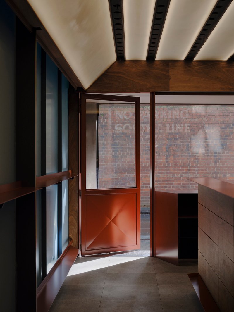View toward the red metal door opening onto the brick courtyard under the timber canopy