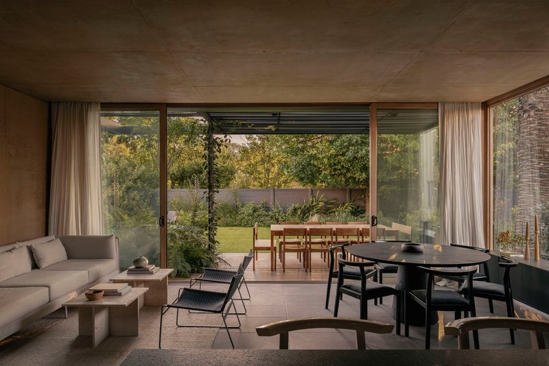 Open plan interior with floor-to-ceiling glazing framing garden view under exposed concrete ceiling