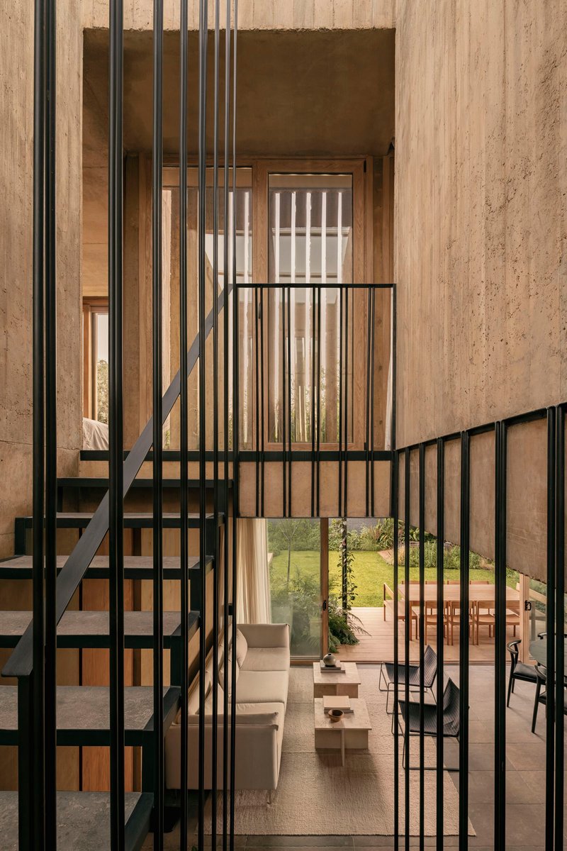Double-height void with black metal staircase and vertical slat screen against board-formed concrete walls