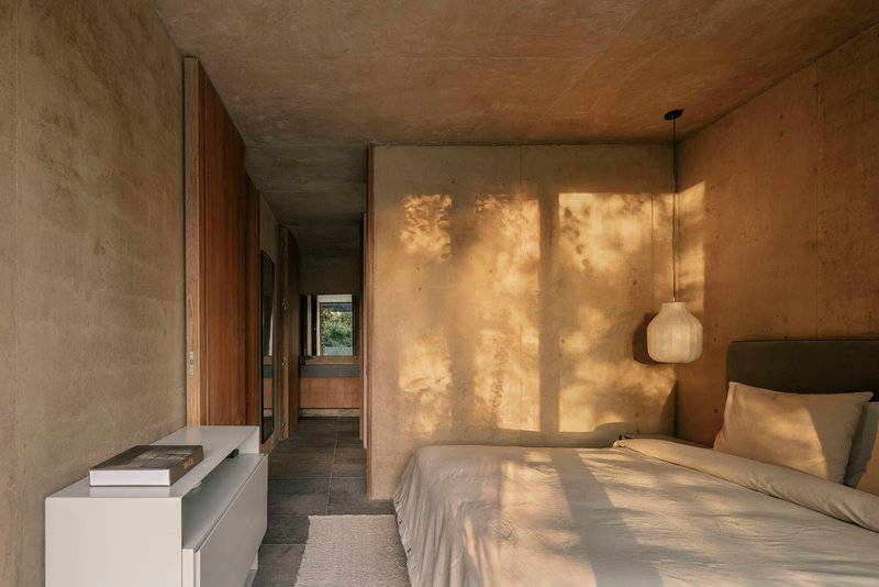 Bedroom corridor with dappled sunlight filtering through exterior louvers onto textured plaster wall