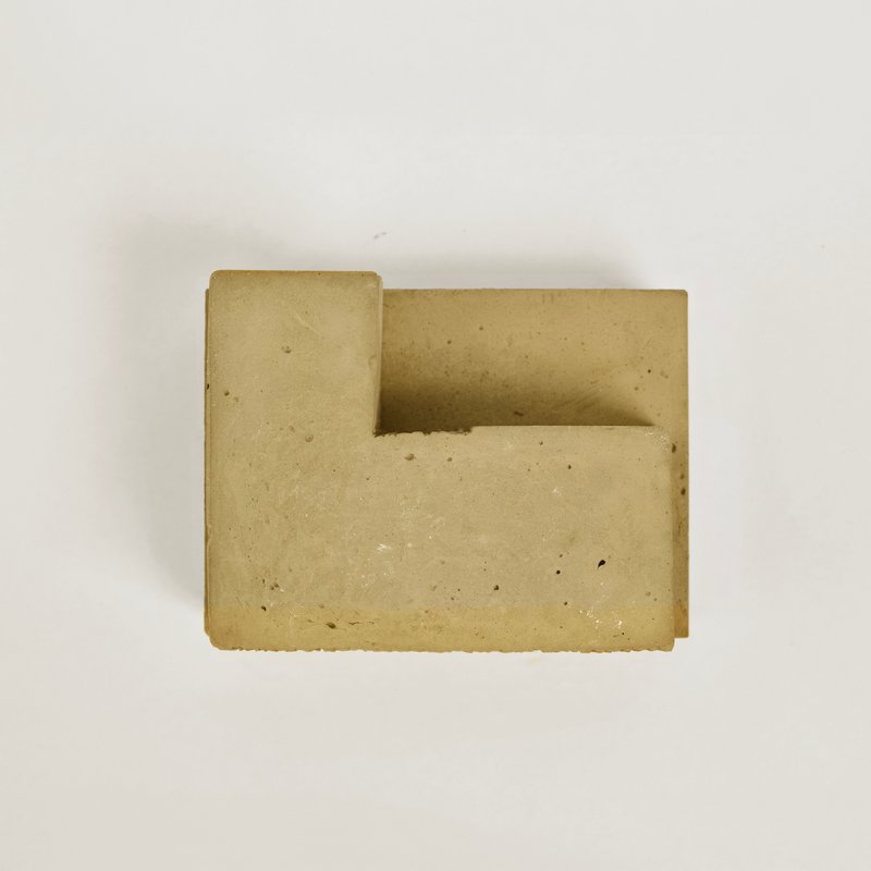 Top-down view of a cast concrete block with a recessed geometric notch on a white surface