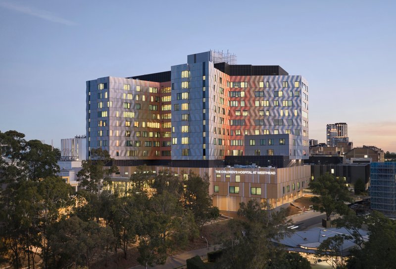 Multi-story hospital building with triangular pattern facade framed by eucalyptus trees at dusk