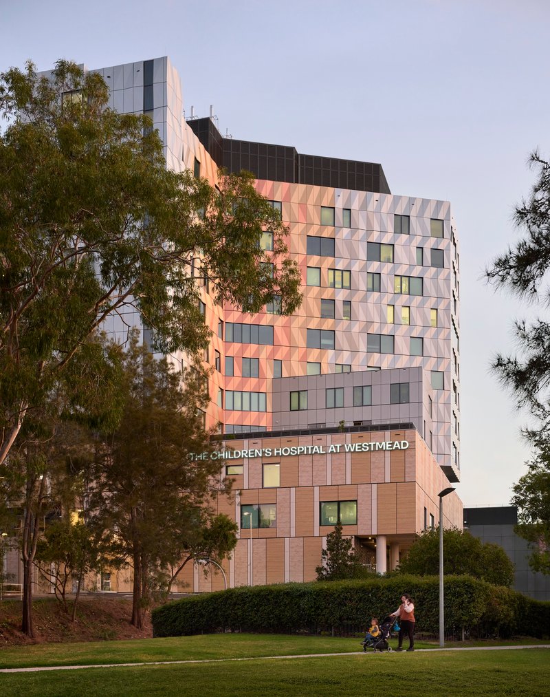 Tower facade with triangular panel cladding in warm and cool tones beside a lawn at twilight