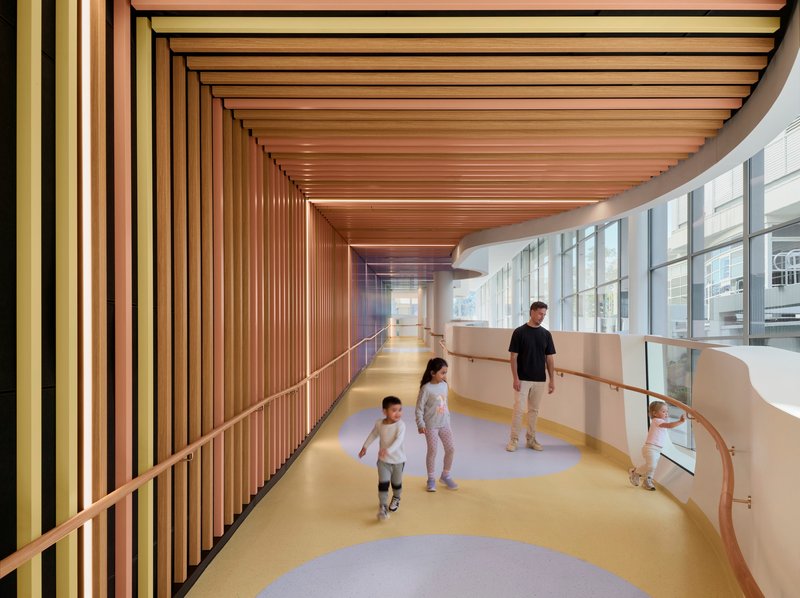 Curved corridor with timber slatted ceiling and yellow flooring as children walk beside glazed wall