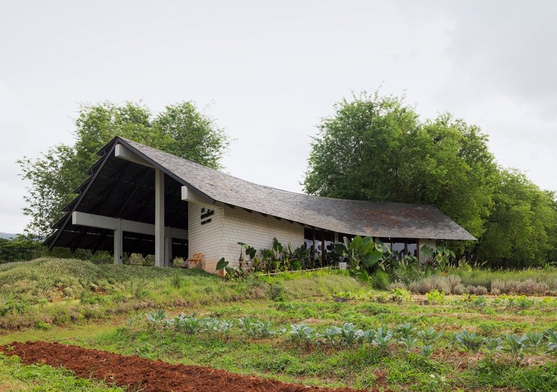 Pitched roof pavilion with brick walls and exposed timber frame amid cultivated vegetable plots