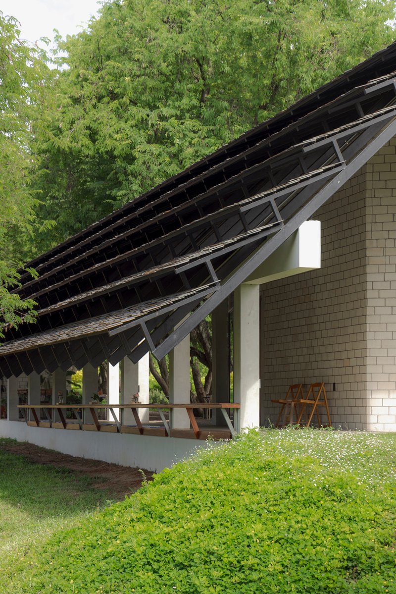 Corner detail of exposed roof structure with timber rafters and white columns beside flowering groundcover
