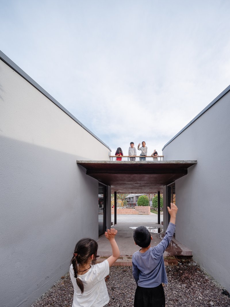 Courtyard view through a timber-roofed passageway with people standing on the rooftop terrace above