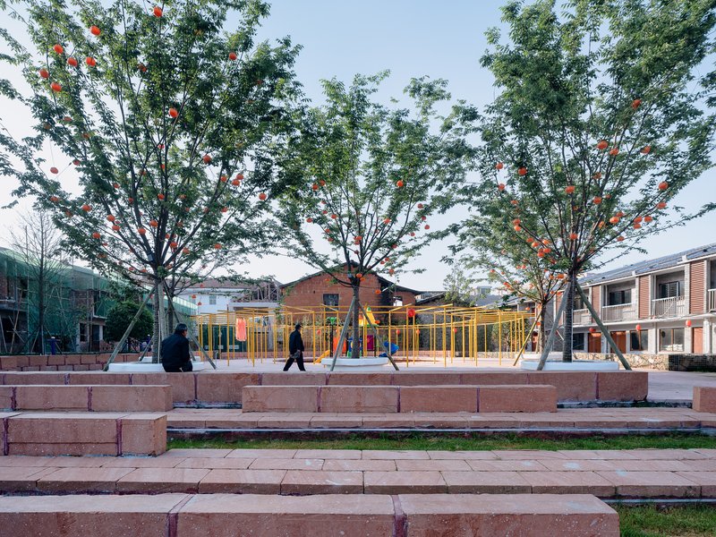 Stepped seating platform with brick risers facing a playground structure and decorative trees