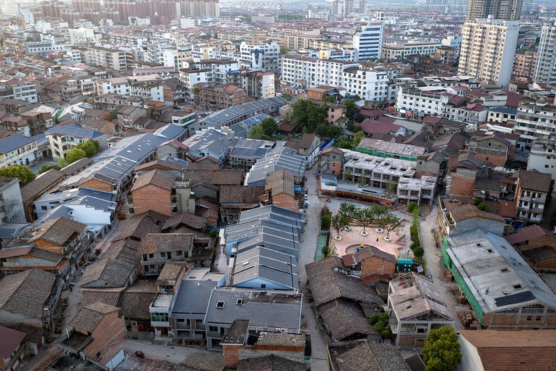 Aerial view of metal-roofed pavilion nestled among low-rise residential blocks in a dense urban neighborhood