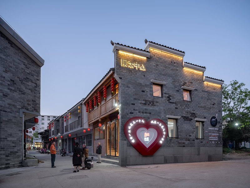 Corner building with grey brick facade and illuminated heart-shaped sign at evening