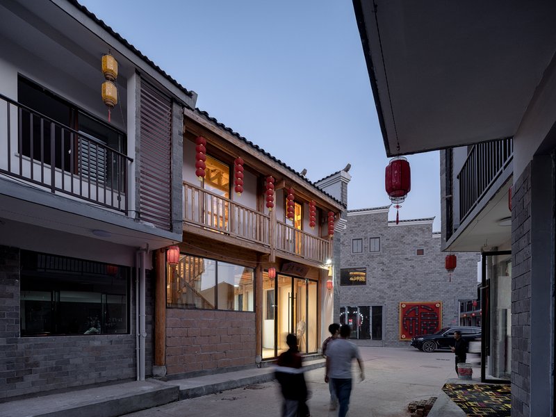 Narrow pedestrian lane between timber-framed building with red lanterns and grey brick structures at dusk