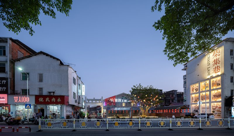 Street view showing mixed commercial buildings with illuminated signage and metal traffic barriers at dusk