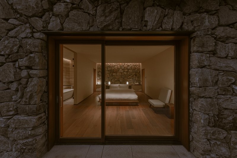 Glass sliding doors set within a rough stone wall opening onto a bedroom at night