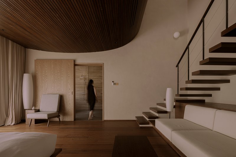 Interior living space with curved timber ceiling and a figure ascending the cantilevered staircase