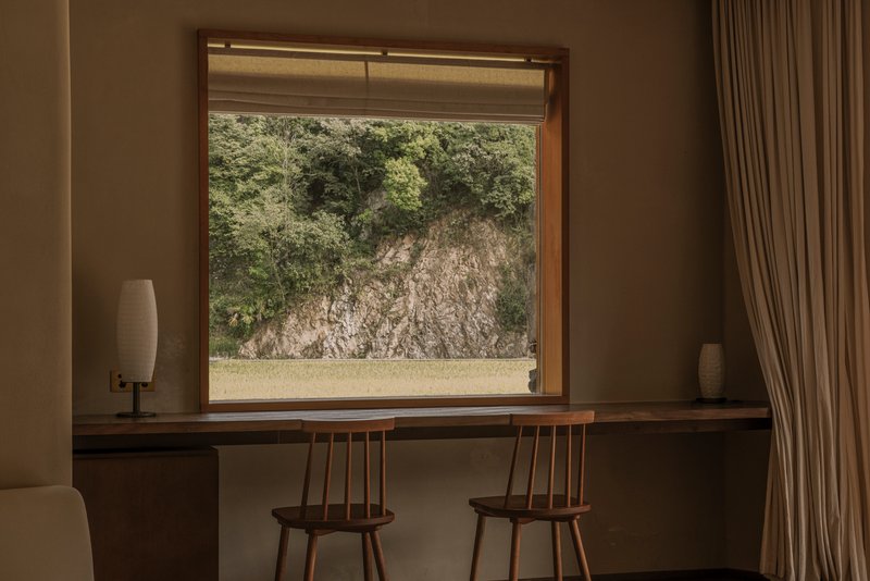 Framed window view of exposed rock outcrop with wooden desk and spindle-back chairs below