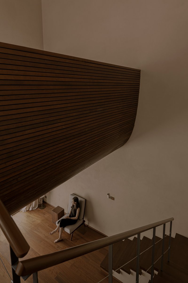 View down stairwell showing curved timber ceiling soffit and a person seated in reading nook
