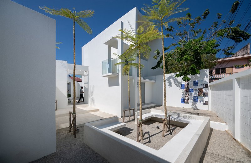 White-walled courtyard with planted tree beds and gravel under a clear blue sky