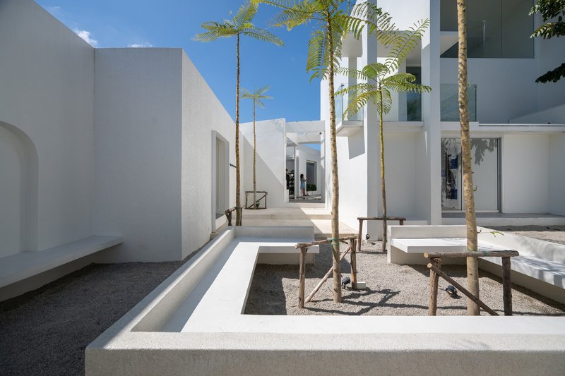 Raised white planting beds with young palm trees in a gravel-paved courtyard