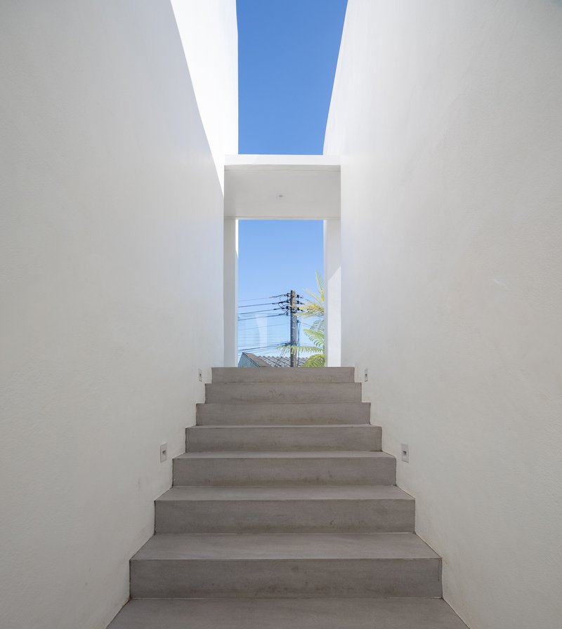 Concrete staircase ascending toward a framed opening and skylight with blue sky beyond