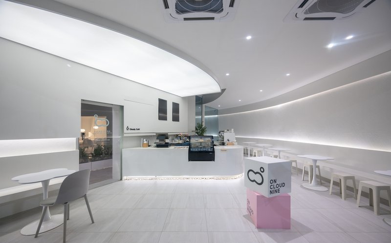 Interior of a cafe with curved counter, continuous LED cove lighting and white seating under recessed ceiling fixtures