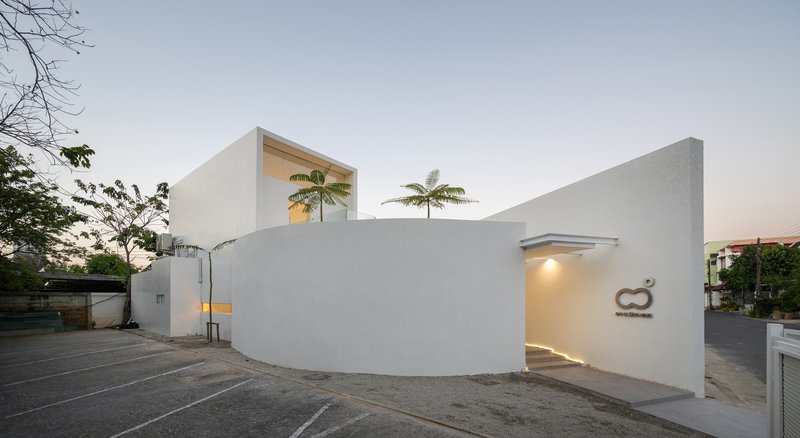 Street-facing facade with curved white stucco wall and recessed entry beneath palm trees at dusk