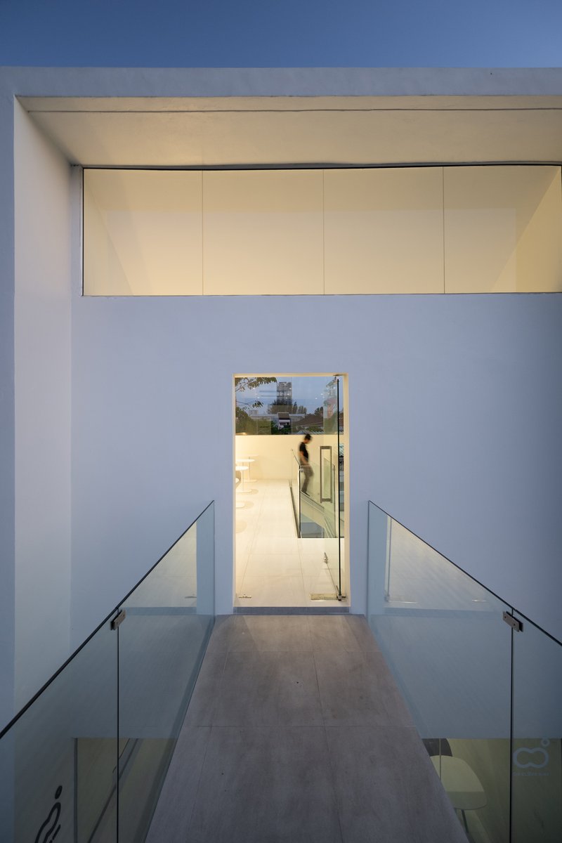 Interior passage with yellow ceiling panels and glass-railed stairs descending toward a glass door at evening