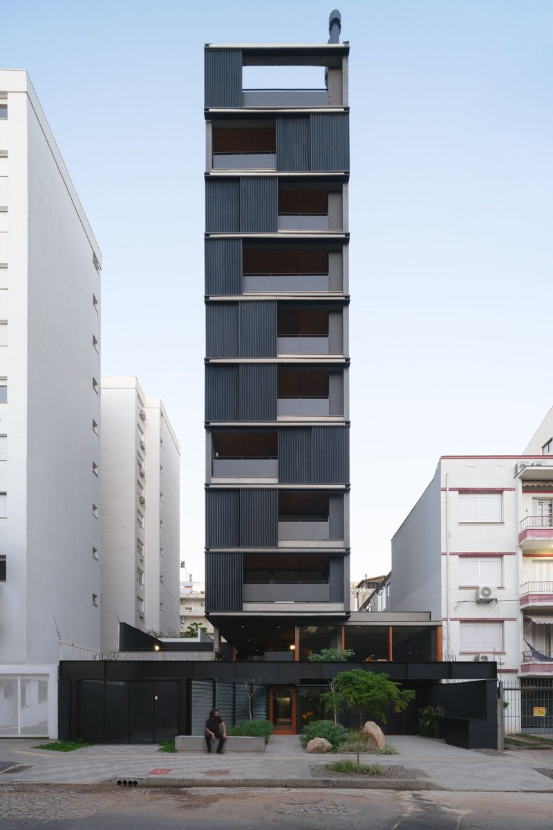 Front elevation of the narrow tower with staggered corrugated metal balconies flanked by white apartment buildings