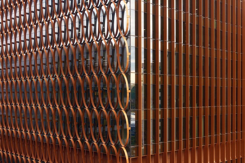 Close-up of the bronze oval screen cladding meeting the vertical timber fin system at a corner