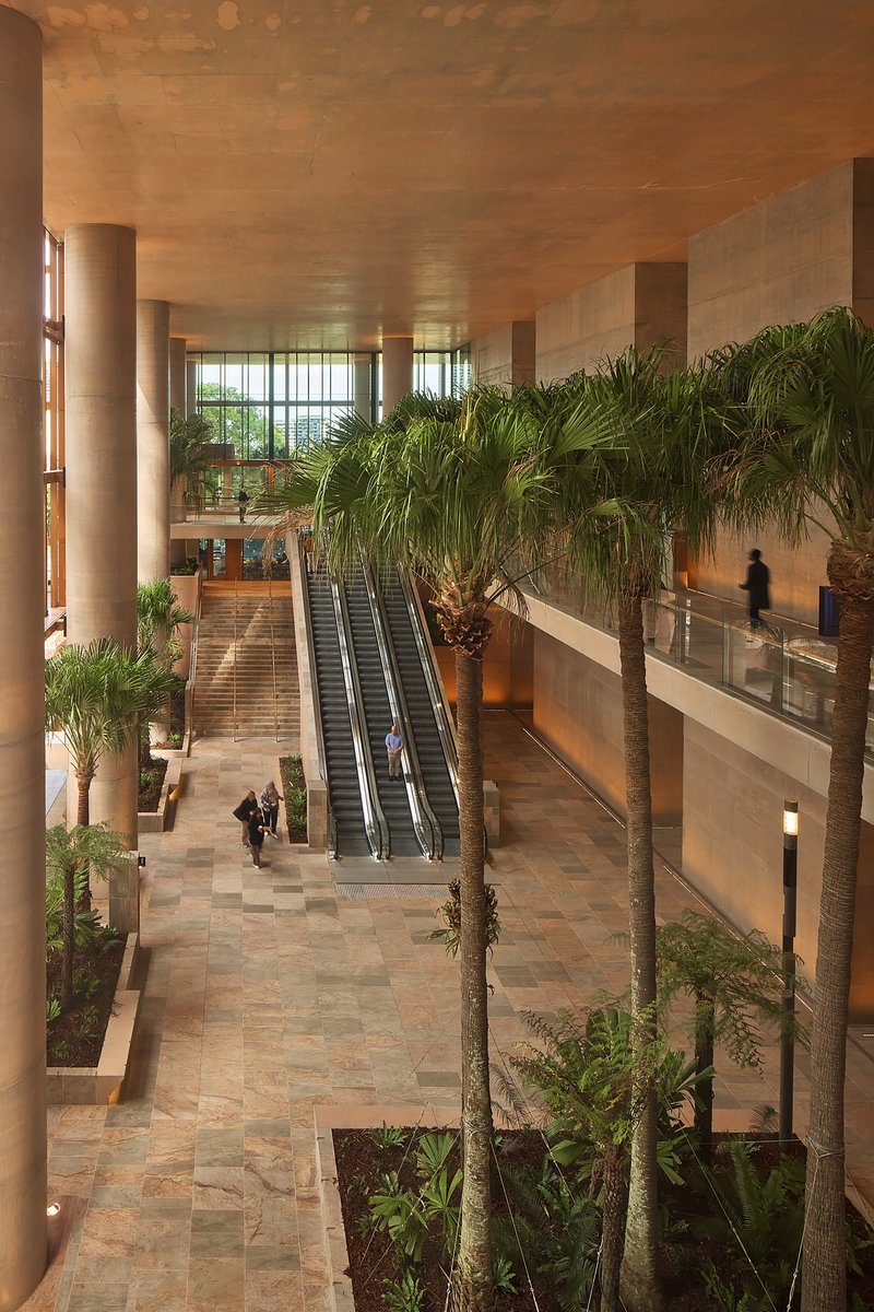 Double-height lobby with escalators flanked by palm trees and stone tile flooring under a coffered ceiling