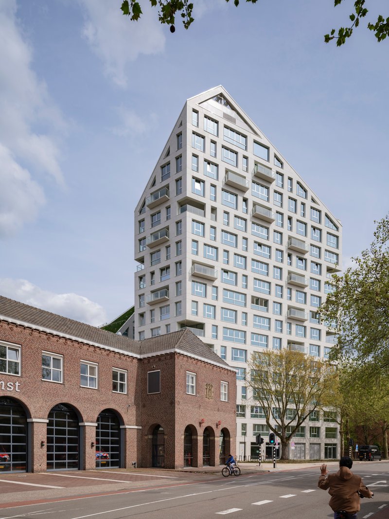Street view of the white tower with recessed balconies rising above a historic brick arcade and a cyclist