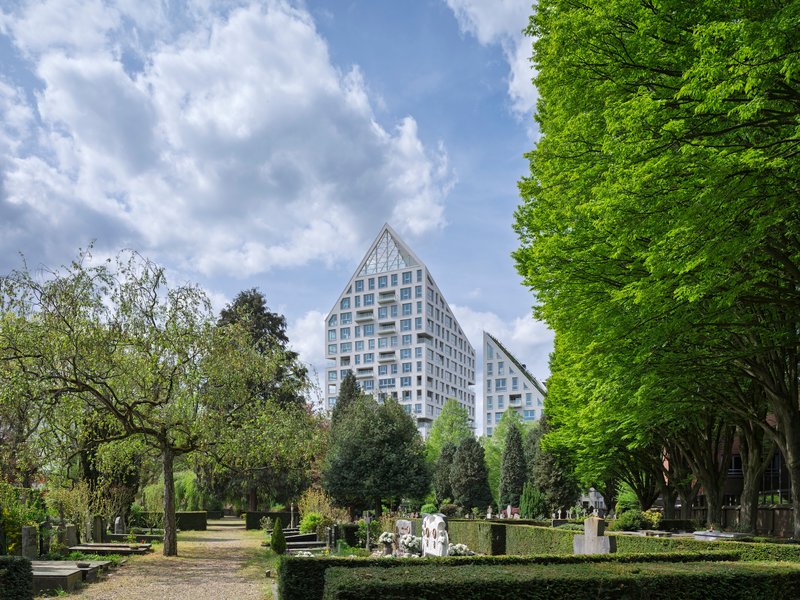 Twin gabled towers rising above a park cemetery with trimmed hedges and spring foliage