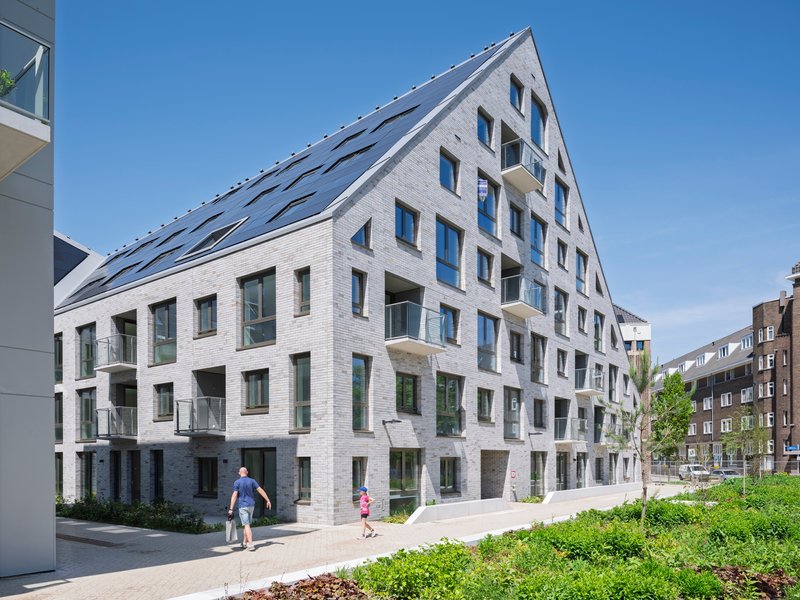 White brick residential facade with staggered balconies and residents walking on the sidewalk