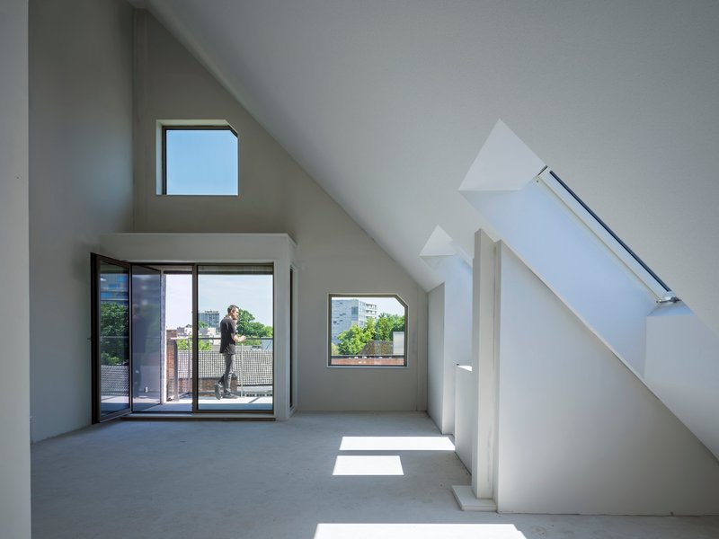 Interior attic space with sloped ceilings, multiple windows, and a figure on the balcony in afternoon light