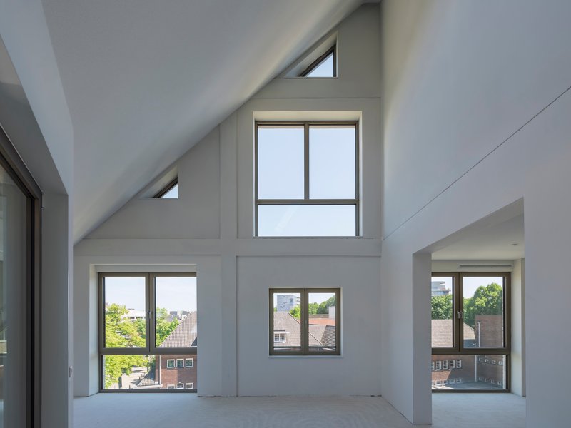 Double-height interior with pitched ceiling, clerestory windows, and varied apertures framing neighboring rooftops