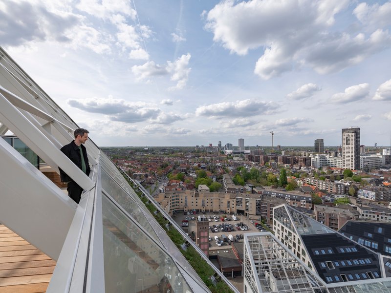 Rooftop terrace with wood decking and sloped glass balustrade overlooking the urban skyline under cloudy skies
