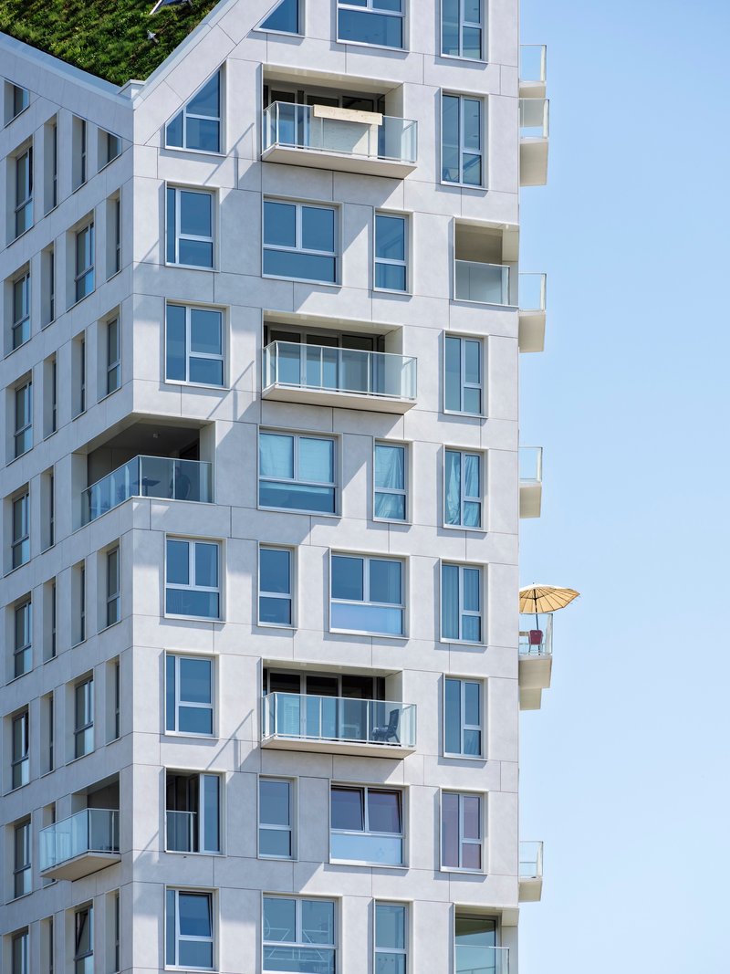 White facade with staggered balconies and glazed openings showing yellow umbrella on upper terrace