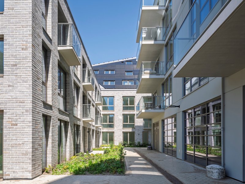 Courtyard passageway between brick facades with projecting balconies and planted beds in bright sunlight