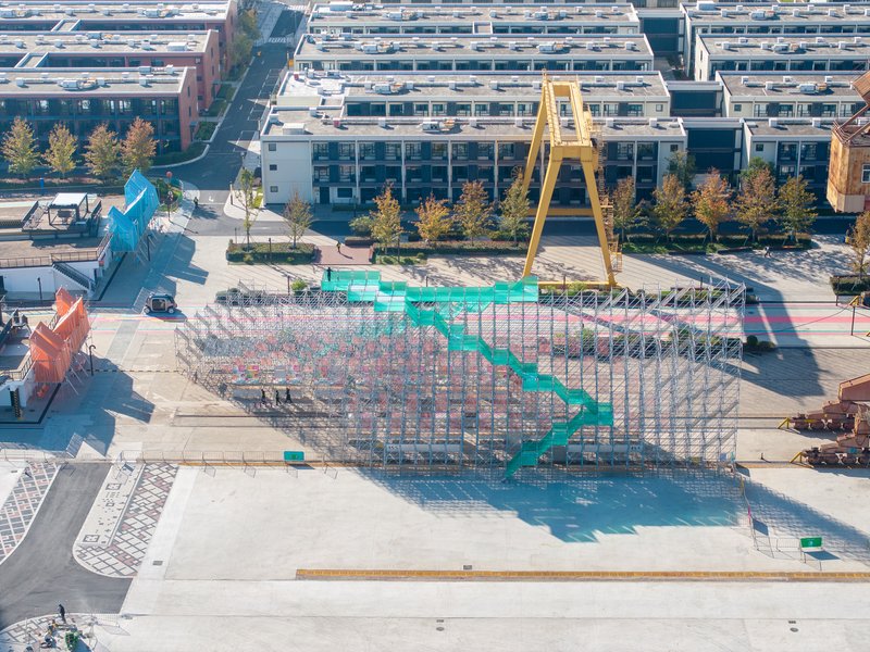 Aerial view of the scaffolding pavilion with turquoise stairway and surrounding low-rise buildings