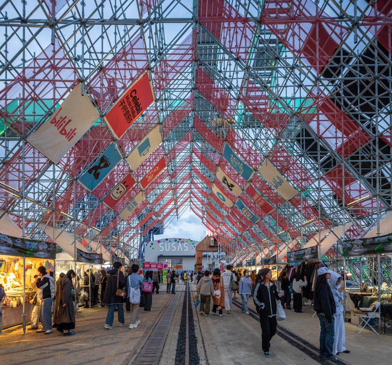 Interior view beneath the tubular truss canopy with hanging banners and market stalls at dusk