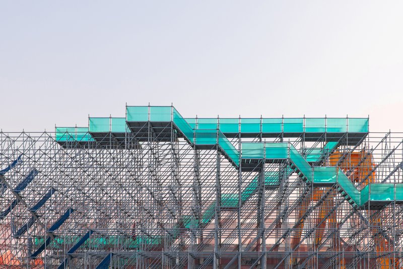 Detail of the turquoise stair platforms supported by the lattice of metal scaffolding tubes