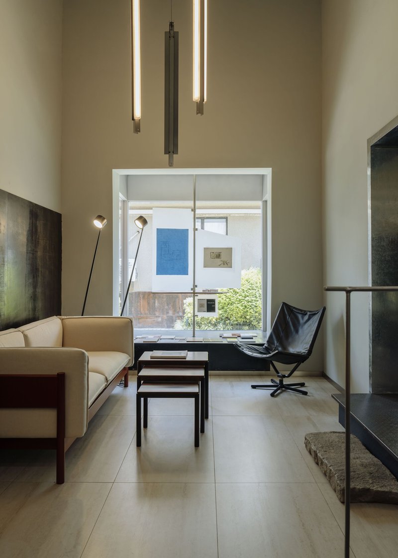 Living room with tall ceiling and tubular pendant lights overlooking a planted courtyard through glazed opening