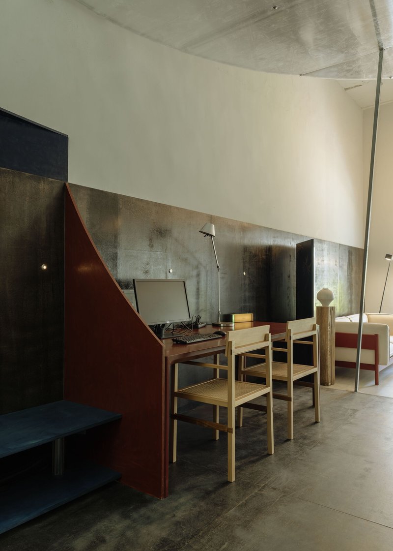 Dining area with timber chairs and maroon partition wall set against variegated metal panel backdrop