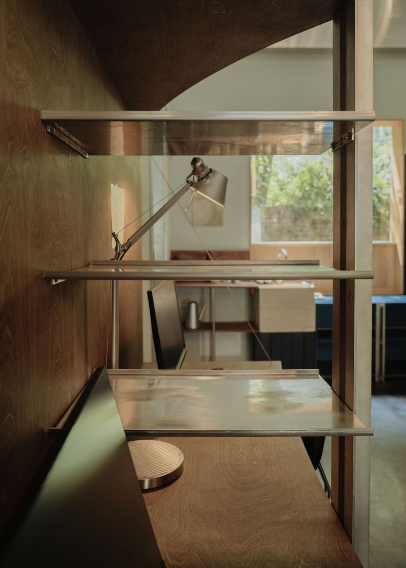 Built-in shelving unit with articulated desk lamp and sliding work surfaces in timber and metal