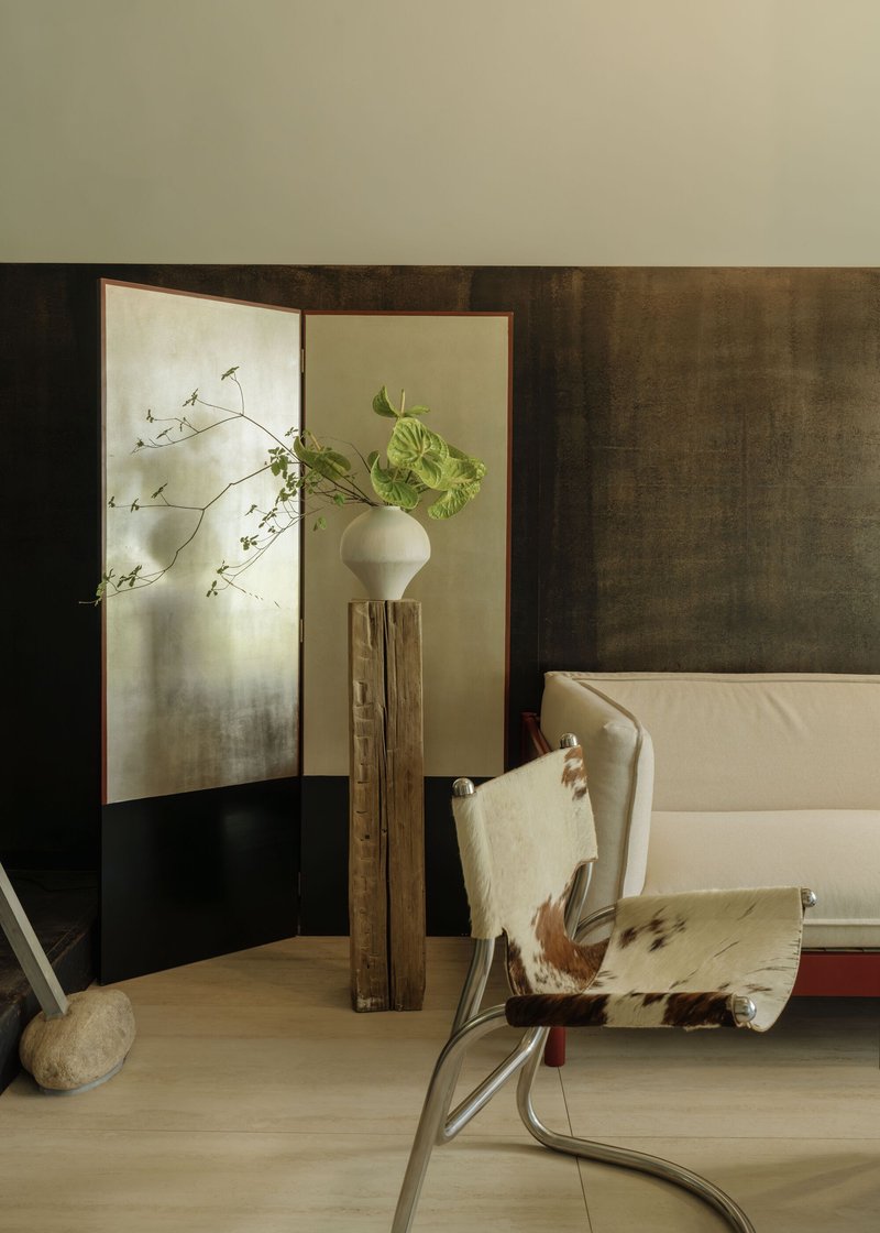 Corner vignette showing folding screen, timber pedestal with vase and cowhide chair in soft light