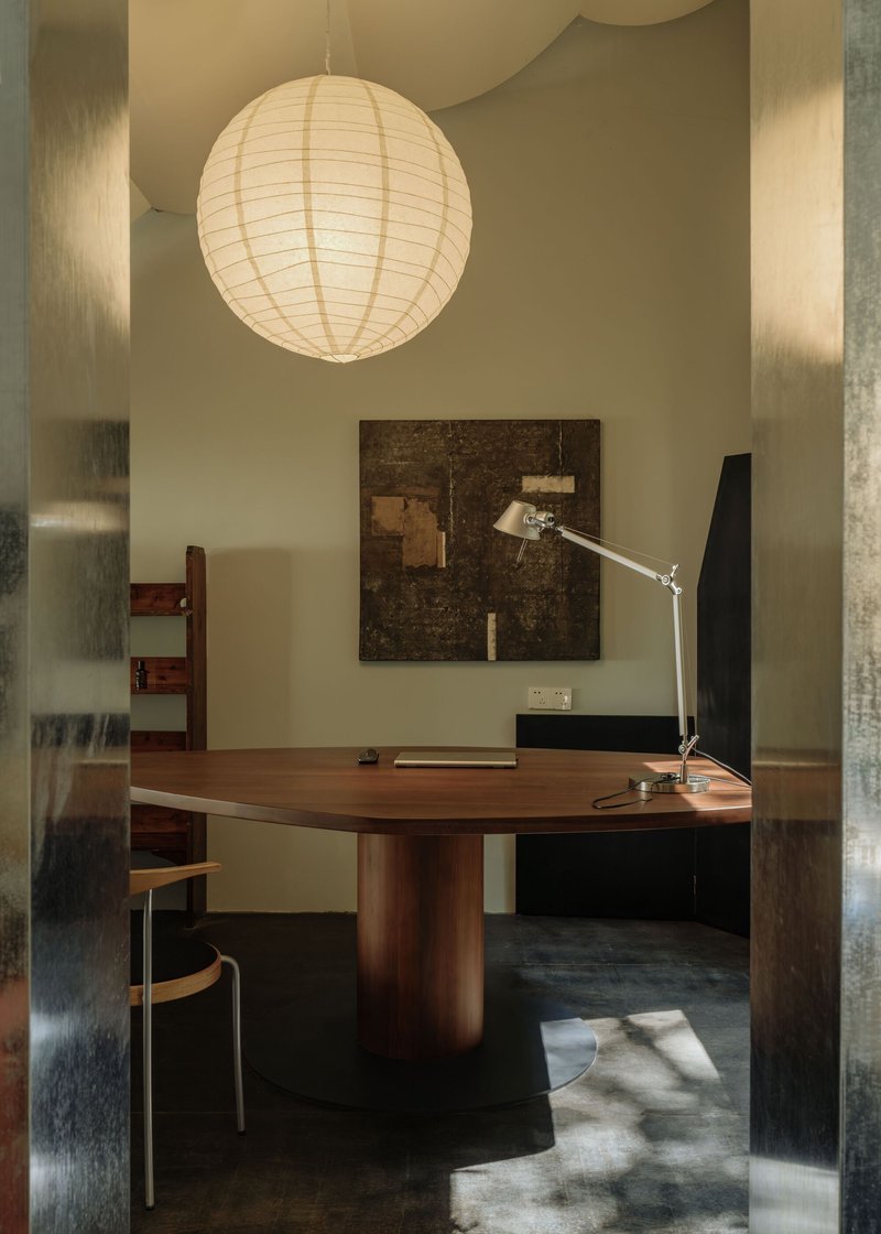 Office with circular walnut table beneath a paper lantern and sunlight falling across dark flooring