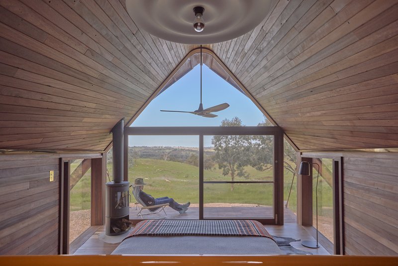 Interior view of timber-lined pitched ceiling with triangular window framing rolling hills and trees