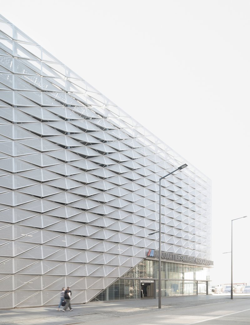Triangulated metal facade with embedded glass panels at street level with a person walking past