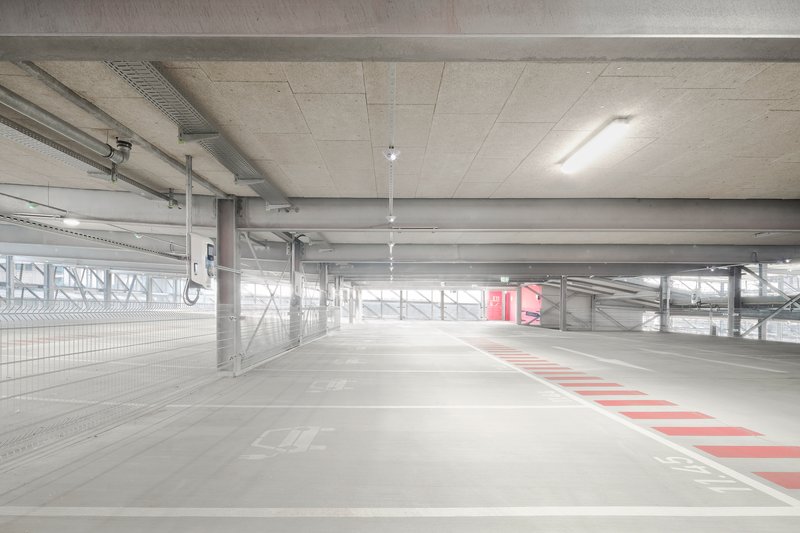 Upper parking level with exposed concrete ceiling beams and metal perimeter screen filtering daylight