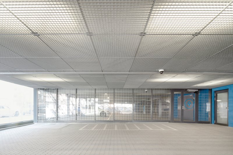 Parking deck interior showing metal mesh ceiling and patterned glass screen with bicycles visible outside