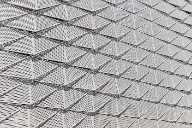 Close-up of perforated metal panels with triangulated structural members creating a geometric facade pattern